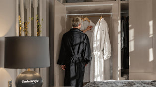  Person weighing luxury robe choices in a sunlit modern bedroom