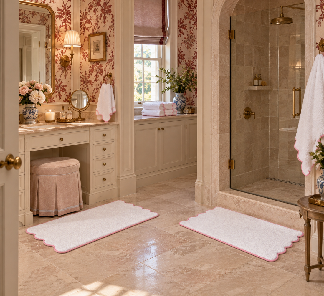 White towels and two scalloped bath mats with pink piping in a bathroom