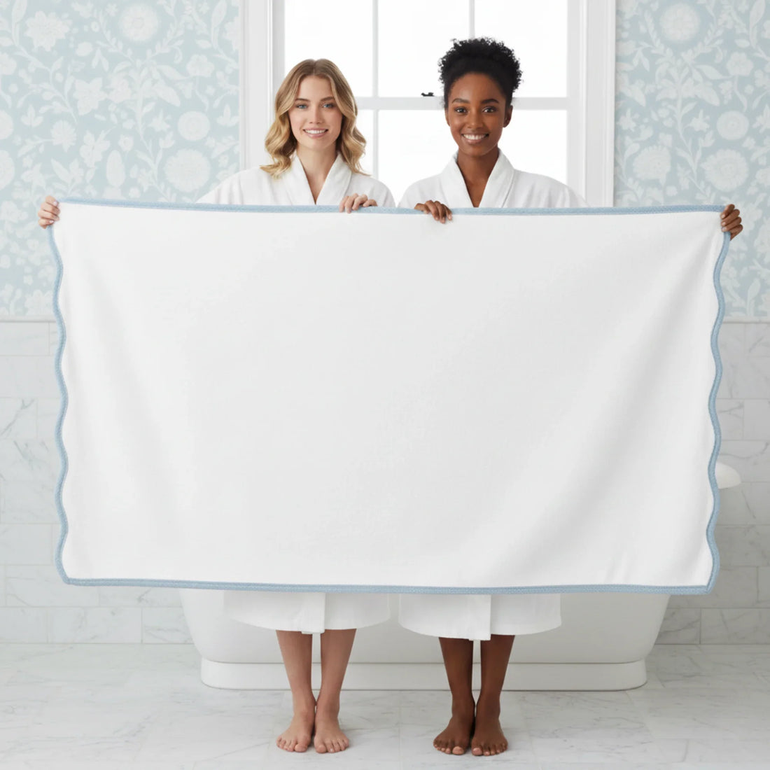 Two women in robes holding oversized white scallop piping bath sheet with blue trim for luxurious spa-quality comfort - Lotus Linen