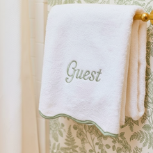  White towel with 'Guest' embroidery on a decorative green and beige background