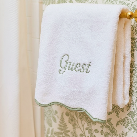 White towel with 'Guest' embroidery on a decorative green and beige background
